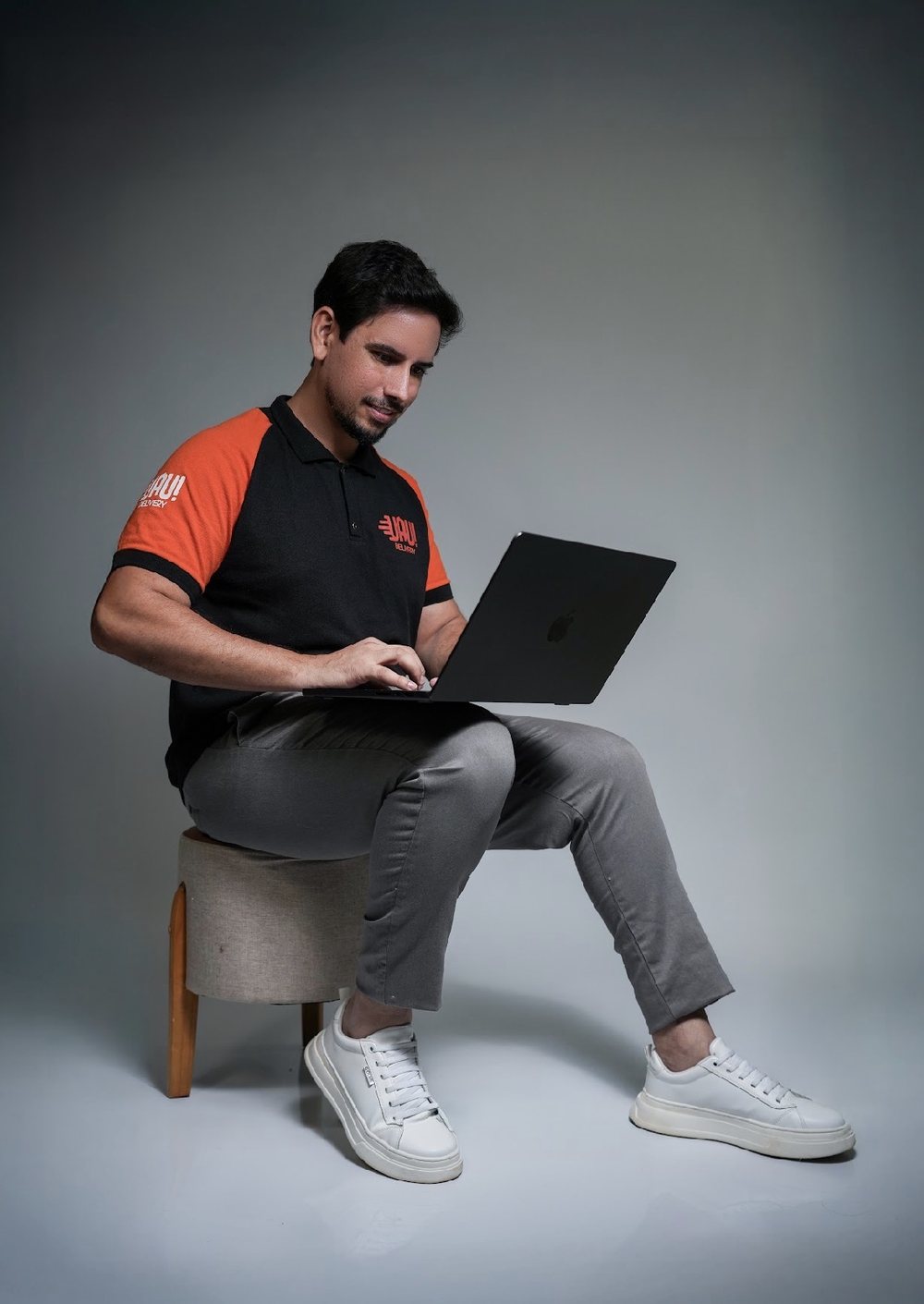 Jansen Rodrigues, fundador do Uau! Delivery, de uniforme da marca, trabalhando em um notebook